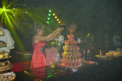 Une femme verse du champagne dans une pyramide de coupes lors d'une réception festive avec éclairage coloré.