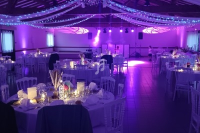 Salle de réception décorée avec des guirlandes lumineuses, tables dressées et éclairage violet tamisé.