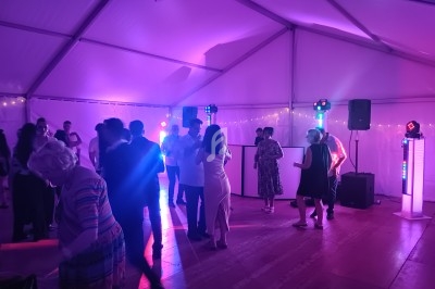 Personnes dansant et discutant sous une tente éclairée par des lumières colorées lors d'un événement festif.