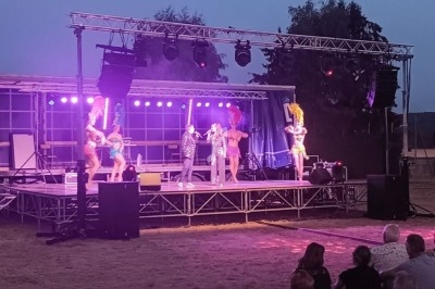 Spectacle en plein air avec danseuses en costumes colorés sur une scène éclairée, devant un public assis.