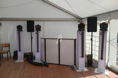 Équipement de sonorisation et éclairage installé sous une tente, avec enceintes, projecteurs et pupitre.
