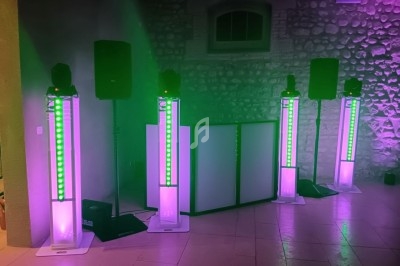 Quatre colonnes lumineuses LED vertes et violettes entourent une table de mixage dans une salle en pierre.