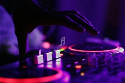 Main posée sur une table de mixage éclairée par des lumières violettes dans une ambiance sombre.