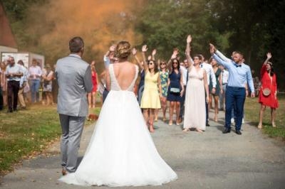Un couple de mariés fait face à un groupe d'invités levant les bras lors d'une célébration en extérieur.