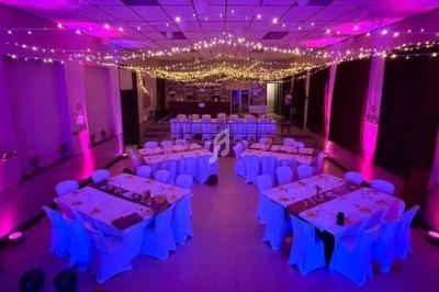 Salle de réception décorée avec des guirlandes lumineuses au plafond, tables dressées et éclairage rose.