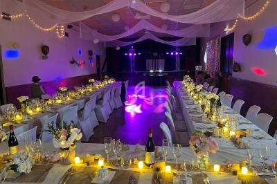 Salle de réception décorée pour un mariage, avec tables alignées, bougies, fleurs et éclairage tamisé.