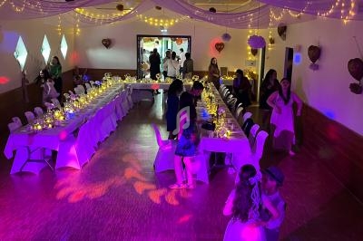 Salle décorée pour une réception avec des tables illuminées, des invités discutant et des personnes dansant au premier plan.