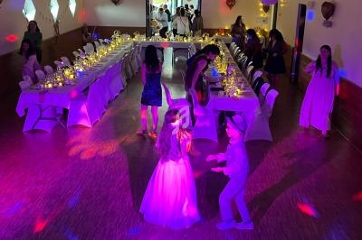 Salle décorée pour une réception avec des tables illuminées, des invités et des enfants dansant sous des lumières colorées.