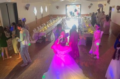 Des invités dansent dans une salle décorée pour une fête, avec des tables dressées et des lumières colorées.