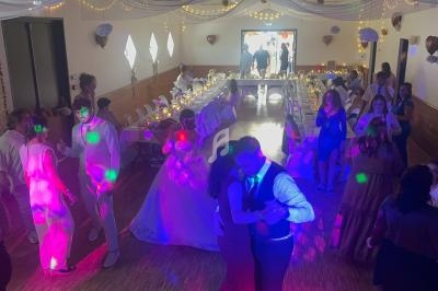 Salle de réception décorée, avec des invités dansant sous des lumières colorées et des tables dressées en arrière-plan.