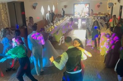 Des invités dansent et discutent dans une salle décorée pour une réception, avec des lumières colorées et des tables…