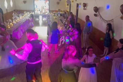 Des invités dansent dans une salle de réception décorée, avec des tables dressées et des lumières colorées.