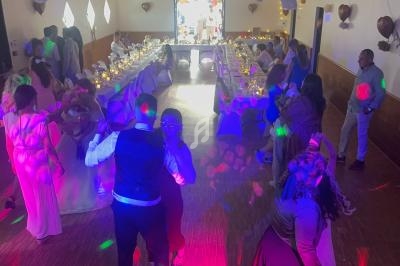 Salle de réception avec des invités dansant sous des lumières colorées, tables décorées en arrière-plan.