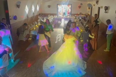 Un couple de mariés danse au centre d'une salle décorée, entouré d'invités et d'effets lumineux colorés.