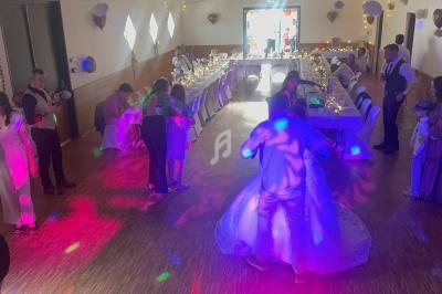 Des invités dansent sur une piste éclairée de lumières colorées lors d'une réception de mariage dans une salle décorée.