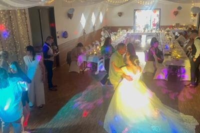 Un couple danse au centre d'une salle décorée pour un mariage, entouré d'invités et de lumières colorées.