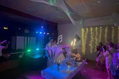 Un homme souffle des bougies sur un gâteau lors d'une fête, entouré de décorations lumineuses et d'invités.