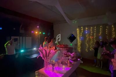 Salle décorée pour une fête avec guirlandes lumineuses, table ornée de fleurs et éclairage coloré.