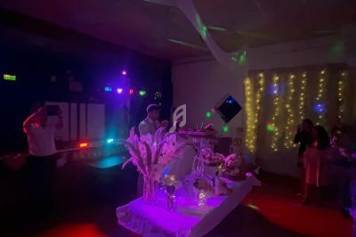 Salle décorée pour une fête avec guirlandes lumineuses, table ornée de fleurs et invités dans une ambiance tamisée.