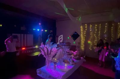 Salle faiblement éclairée avec des décorations lumineuses, une table ornée de fleurs et des invités debout.