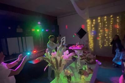 Salle décorée avec des guirlandes lumineuses, table ornée de fleurs et desserts, personnes dansant sous des éclairages…