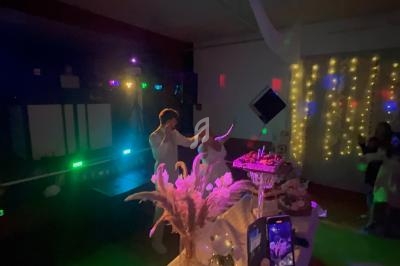 Un couple danse sous des lumières colorées dans une salle décorée avec des guirlandes lumineuses et des fleurs.