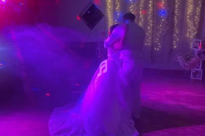 Un couple en tenue de mariage danse sous des lumières colorées dans une salle décorée de guirlandes lumineuses.