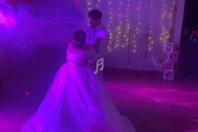 Un couple en tenue de mariage danse sous des lumières colorées et une décoration lumineuse en arrière-plan.