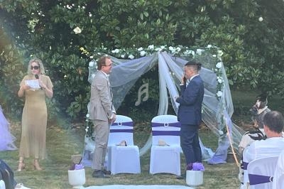 Deux personnes échangent des vœux devant une arche décorée de fleurs blanches, lors d'une cérémonie en plein air.