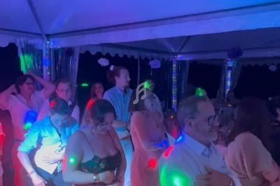 Des personnes dansent sous une tente éclairée par des lumières colorées lors d'un événement en soirée.