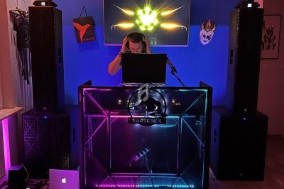 DJ mixant derrière une console lumineuse avec des haut-parleurs et des décorations murales en arrière-plan.
