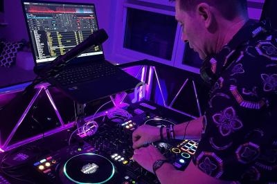 Un DJ mixe de la musique sur une table de mixage éclairée, avec un ordinateur portable affichant des pistes audio.