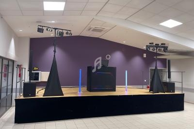 Scène intérieure avec équipement de sonorisation et éclairage, incluant une table de DJ et des projecteurs.