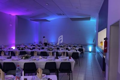 Salle de réception décorée avec des tables dressées pour un événement, éclairage d'ambiance violet et bleu.