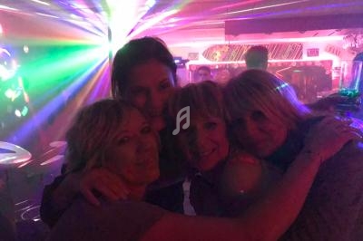 Quatre personnes s'enlaçant dans un environnement festif avec des lumières colorées en arrière-plan.