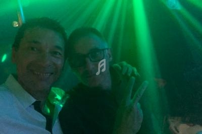 Deux personnes souriantes posent sous des lumières vertes dans un environnement sombre, probablement en soirée.