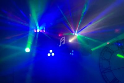 Effets lumineux colorés avec faisceaux verts, bleus et rouges projetés dans une pièce sombre avec une horloge murale visible.