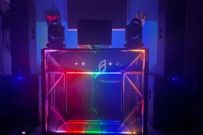Console de DJ éclairée par des lumières LED colorées, entourée de deux grandes enceintes dans une pièce sombre.