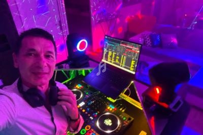 Un DJ souriant devant une table de mixage éclairée, entouré de lumières colorées dans une ambiance festive.