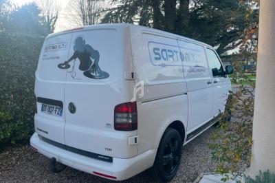 Fourgonnette blanche stationnée dans une allée, avec un logo d'entreprise et des informations visibles sur l'arrière.