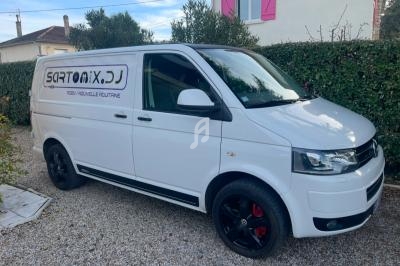 Fourgonnette blanche stationnée sur une allée gravillonnée devant une maison avec des volets roses.