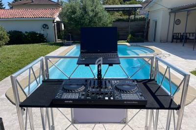Poste de DJ avec contrôleur, ordinateur portable et support, installé près d'une piscine dans un jardin ensoleillé.