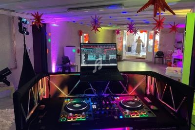 Poste de DJ avec platines et ordinateur dans une salle décorée de lumières colorées et d'étoiles suspendues.