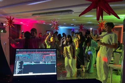 Des personnes dansent dans une salle décorée de lumières colorées et d'étoiles suspendues, vue depuis une table de mixage.