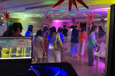 Groupe de personnes dans une salle décorée, éclairée par des lumières colorées, avec une table de buffet et un poste de DJ.