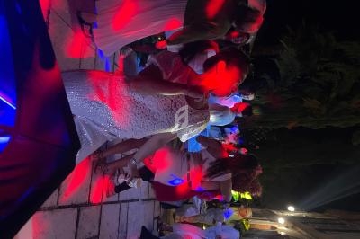 Des personnes dansent en extérieur de nuit sous des lumières rouges et bleues, sur une terrasse entourée de végétation.