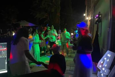 Des personnes dansent en soirée en extérieur, éclairées par des lumières colorées près d'un bâtiment.