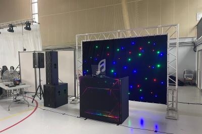 Installation de matériel de sonorisation et éclairage avec une table de mixage et un fond lumineux dans une salle.