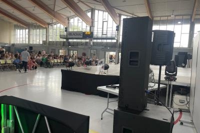 Vue d'une salle polyvalente avec scène, public assis et équipements techniques au premier plan.