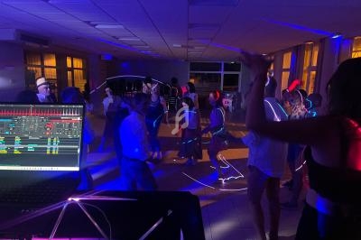 Des personnes dansent dans une salle éclairée par des lumières colorées, avec une table de mixage visible au premier plan.